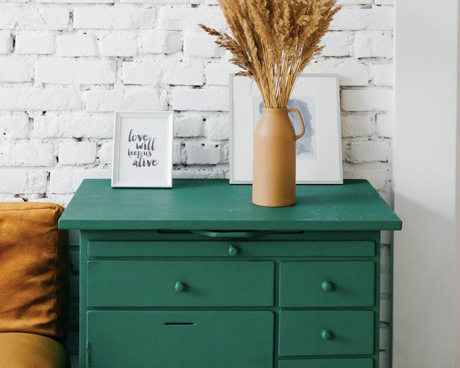 Photo of a green dresser with a golden vase and two white frames